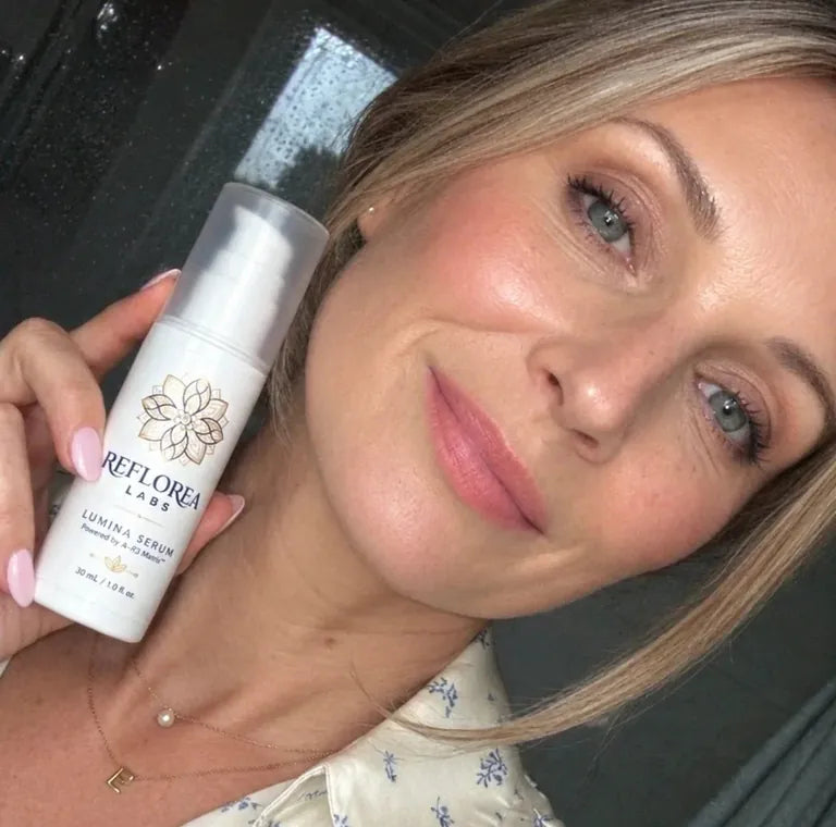 A woman with fair hair holding a bottle of Lumina Serum next to her face