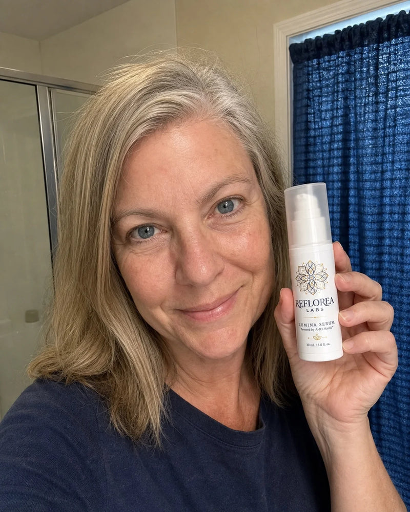 A woman in a navy T-shirt holding a bottle of Lumina Serum in her bathroom