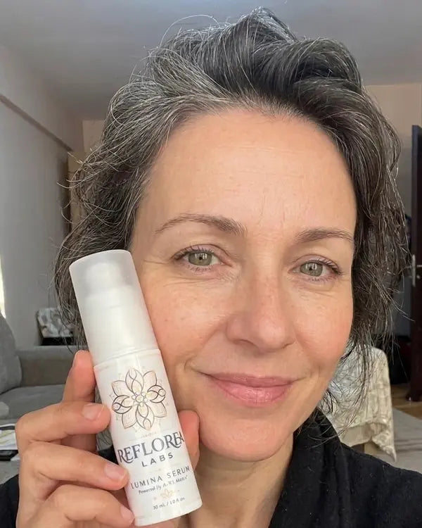 A woman over 40 holding a bottle of Lumina Serum