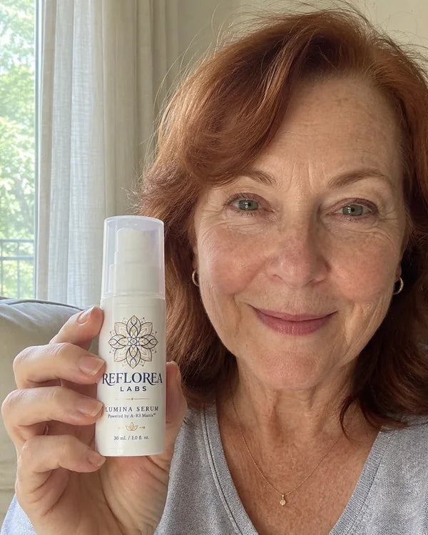 A woman over 40 holding a bottle of Lumina Serum