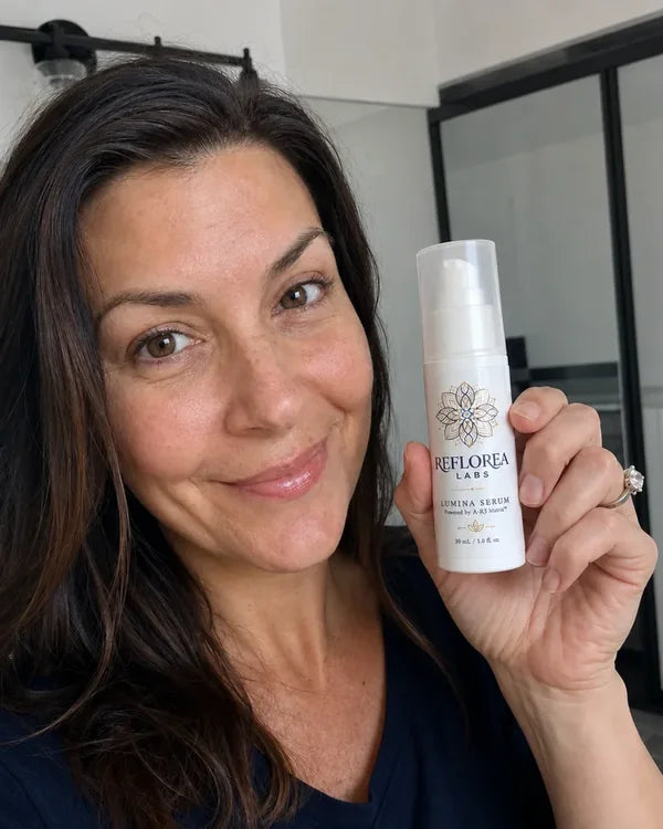 A woman over 40 holding a bottle of Lumina Serum